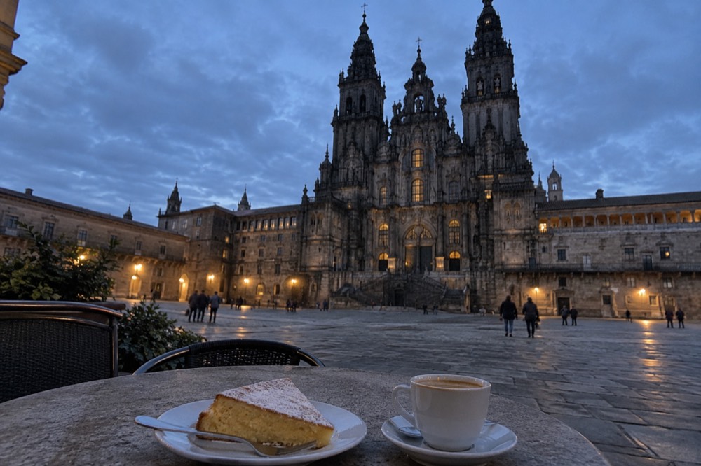 A slice of almond tarta de Santiago beside a small coffee on a stone cafe table