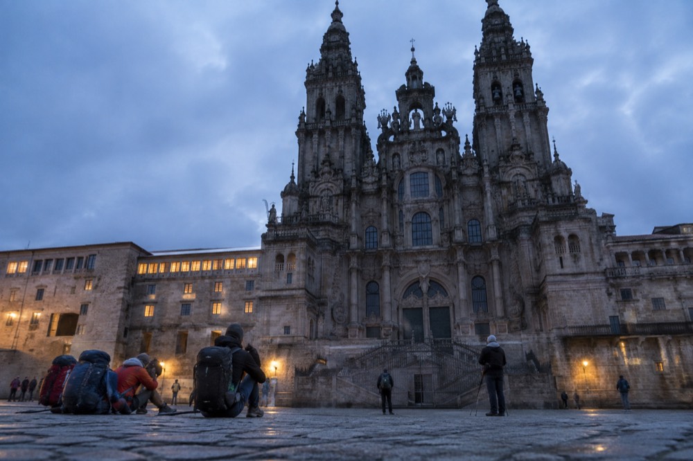 Pilgrims with backpacks and walking sticks resting on the stones near the Cathedral in Santiago de Compostela
