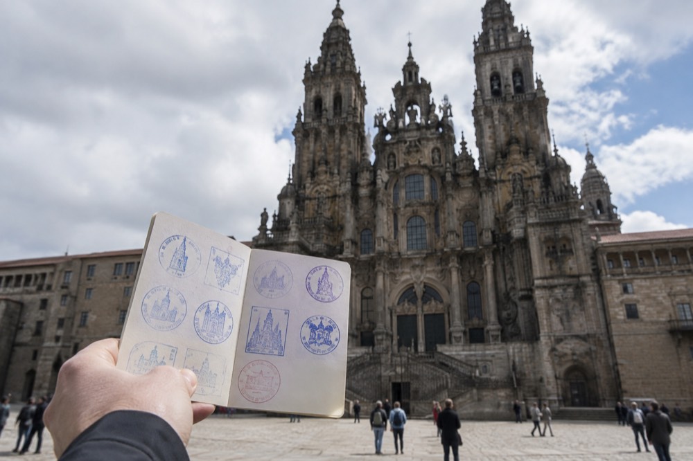 A pilgrim's credential passport held open showing stamped Camino waypoints