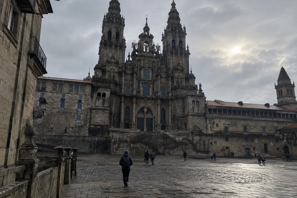 A walker in a rain jacket crossing a stone street in Santiago de Compostela