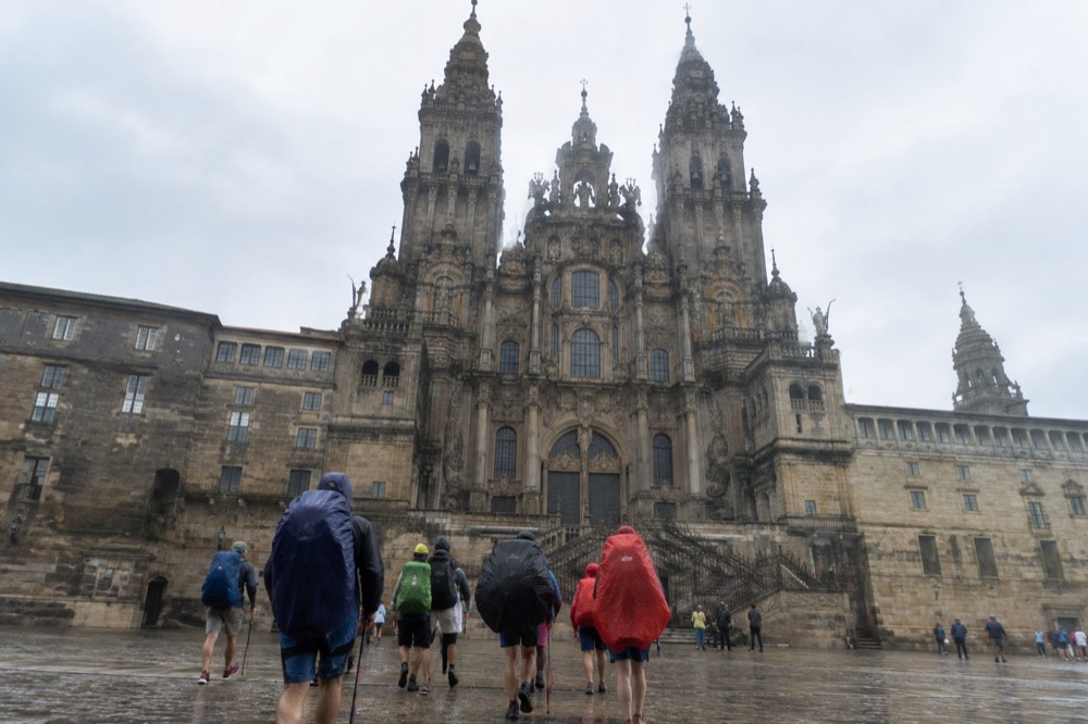Pilgrims in rain gear walking the final Camino stage toward Santiago de Compostela