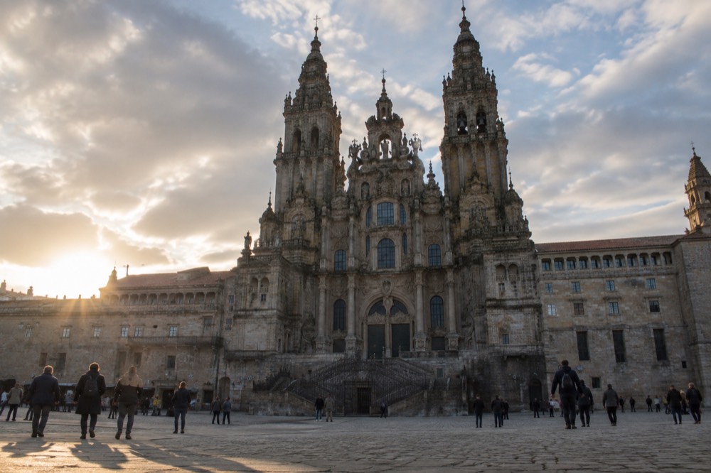 The baroque Obradoiro facade of Santiago de Compostela Cathedral seen across the wide stone plaza at golden hour