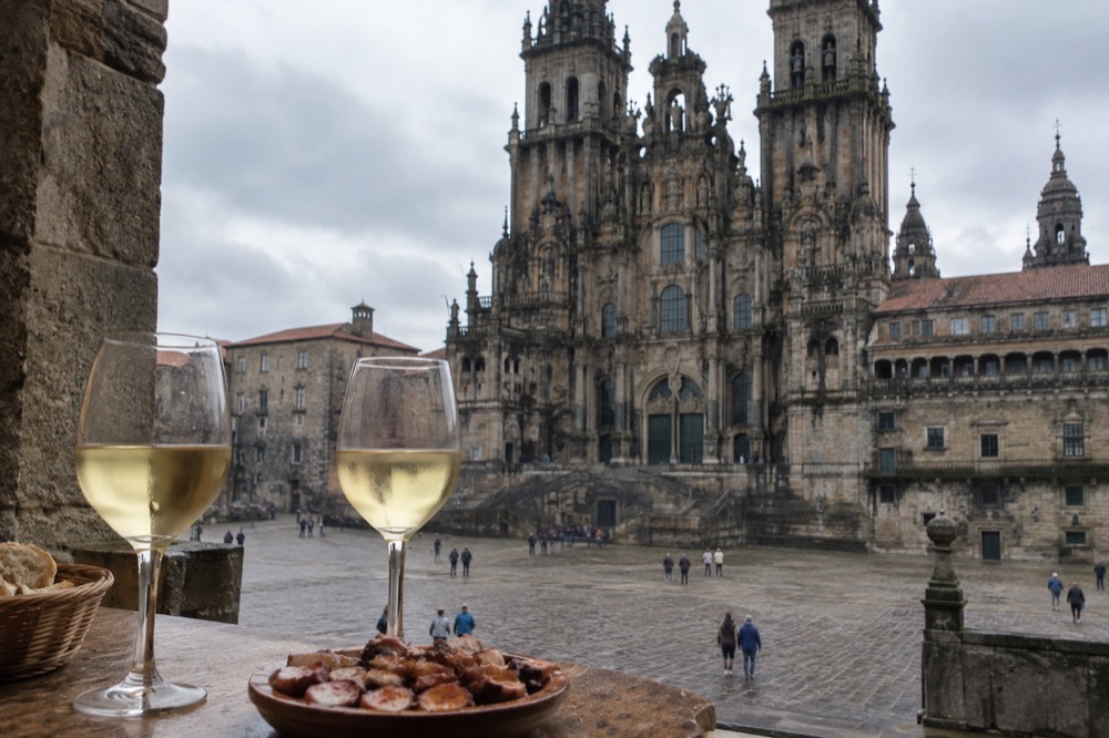 Glasses of pale Galician white wine and a plate of octopus on a wooden bar top in Santiago de Compostela