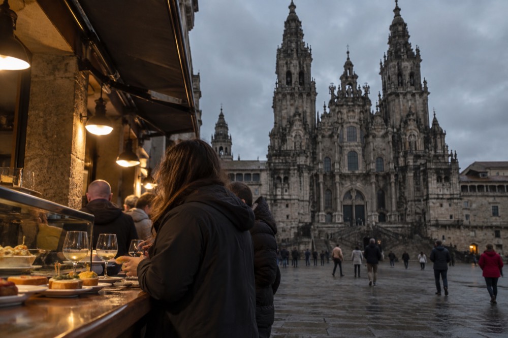 People standing at a tapas bar counter with plates of food in the evening in Santiago de Compostela