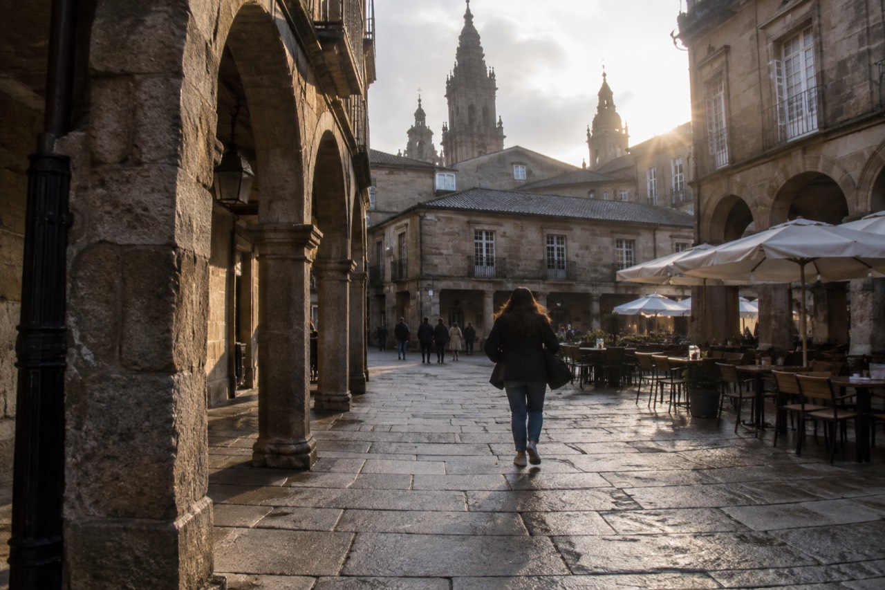 A stone square in the old town of Santiago de Compostela with cafe tables set out beside historic buildings