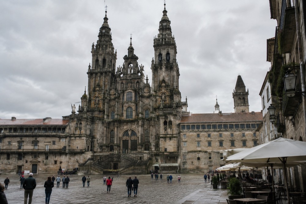 A narrow granite street in Santiago de Compostela lined with restaurant awnings and outdoor tables