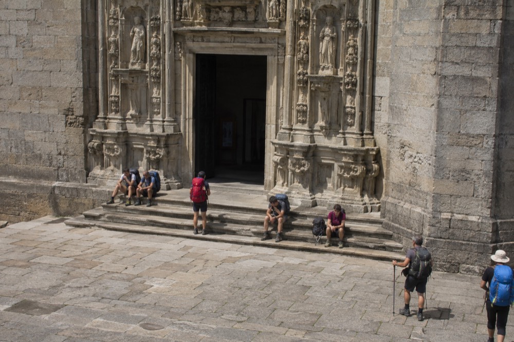 Pilgrims with backpacks resting on stone steps near a baroque church portico