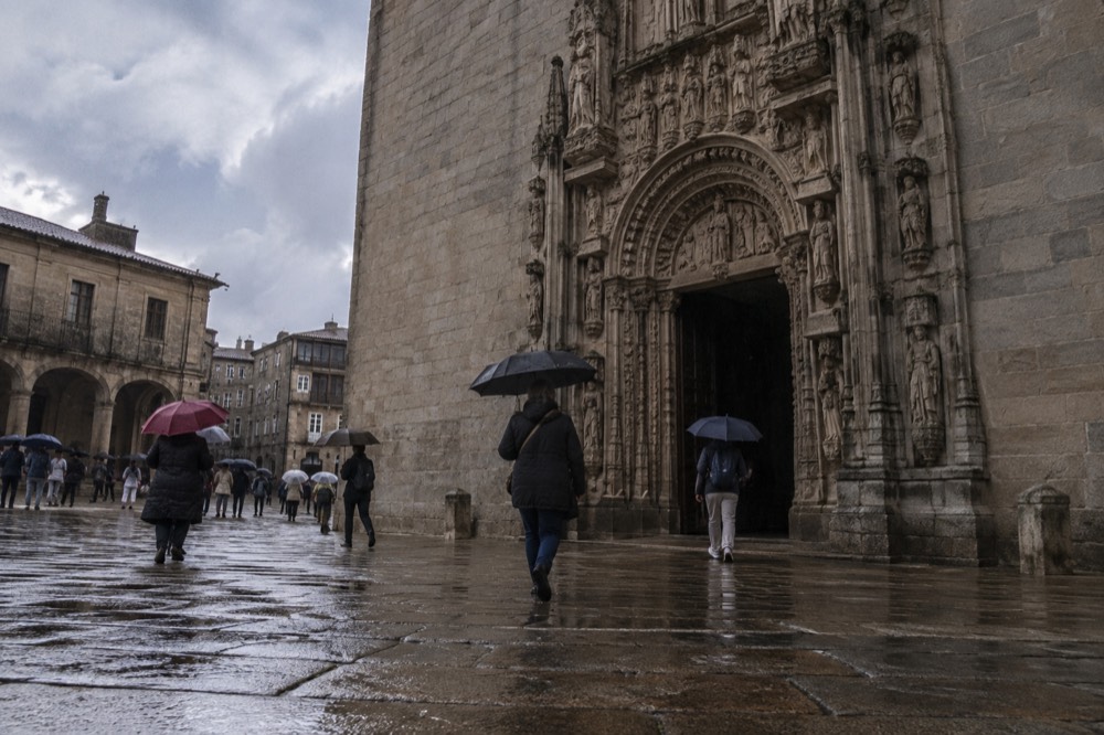 Rain-washed granite square with people under umbrellas beside arcades