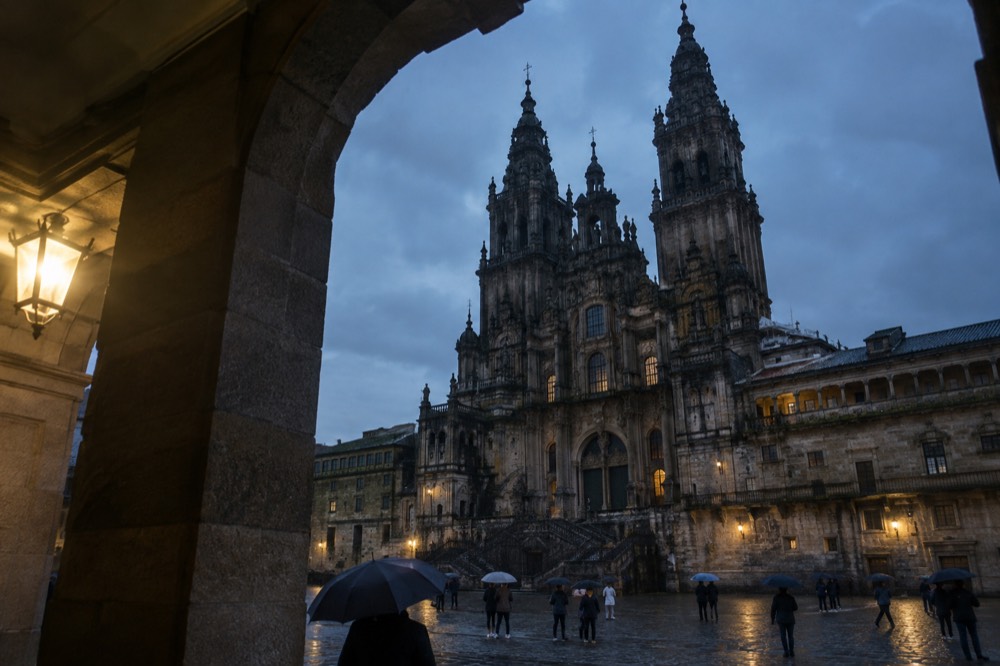 Dark wet stone facade of the cathedral seen from a colonnade with umbrellas below