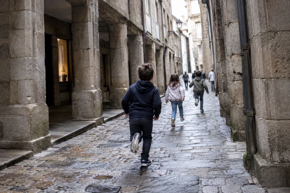 Children running down a narrow cobbled lane lined with stone buildings in the old town