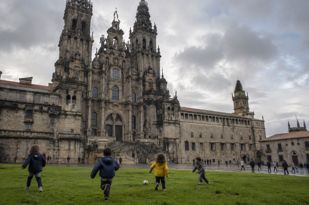 Children playing on open grass with the cathedral skyline of Santiago de Compostela in the background
