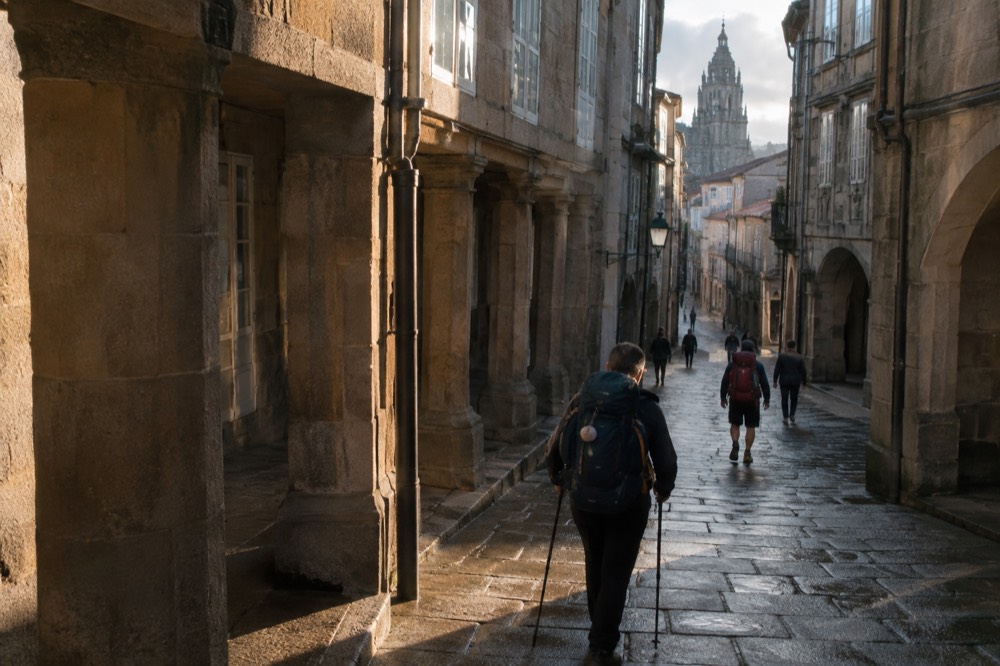 Pilgrims with backpacks arriving in a narrow granite street in the old town of Santiago de Compostela
