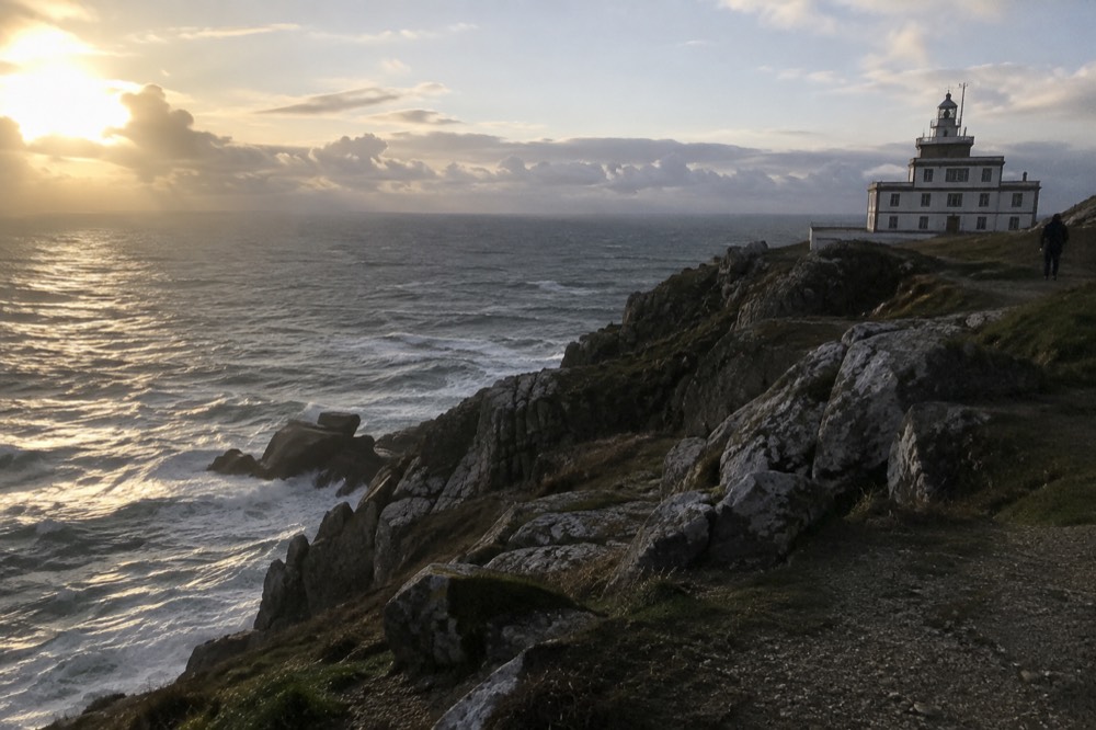 A white lighthouse on a rocky Atlantic headland above crashing waves at Fisterra