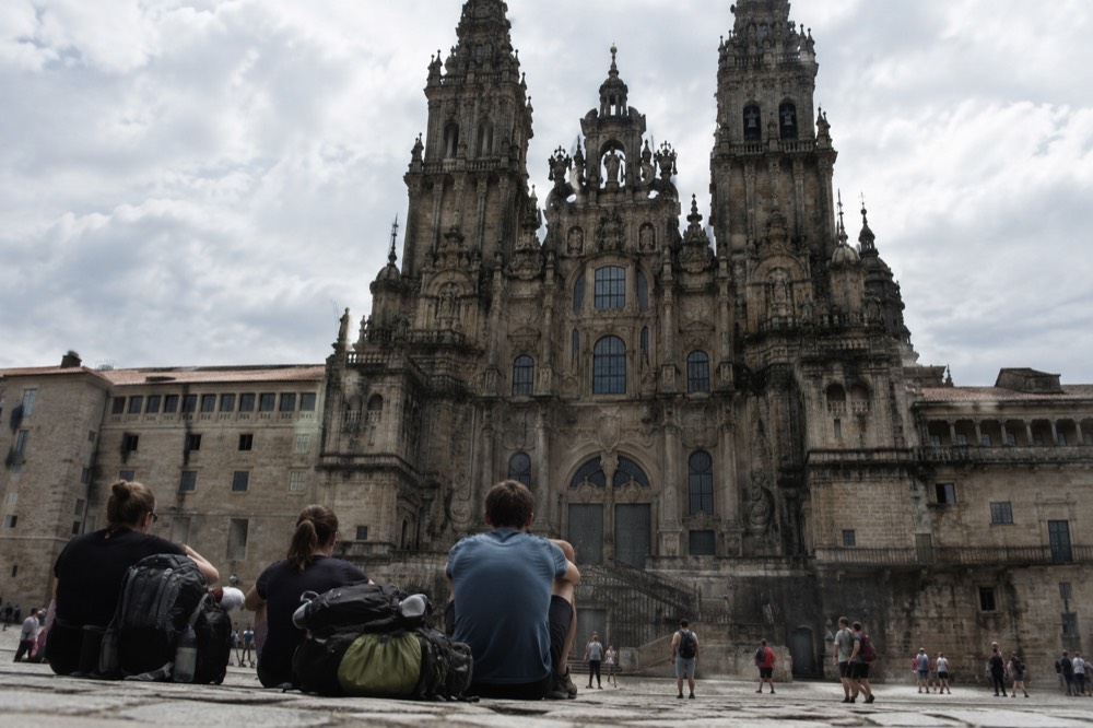 Pilgrims resting with backpacks on the stone steps in front of the Cathedral