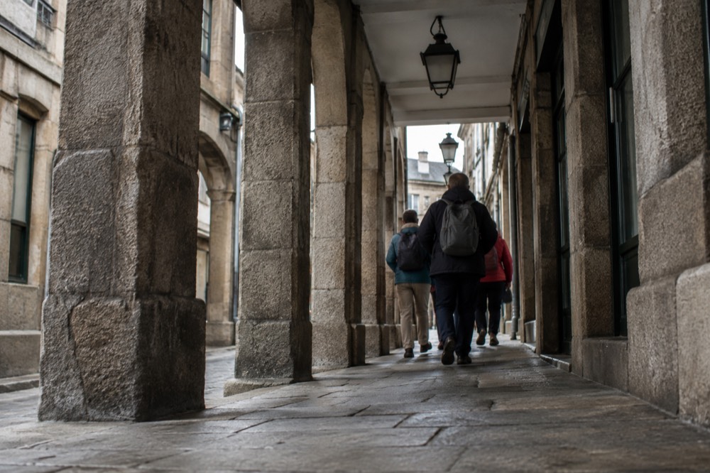 A guide leading walkers through a narrow granite arcade in the old town of Santiago de Compostela