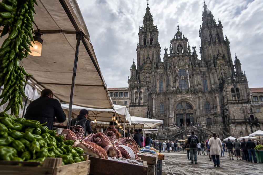 A busy market stall displaying padron peppers and fresh octopus in Santiago de Compostela